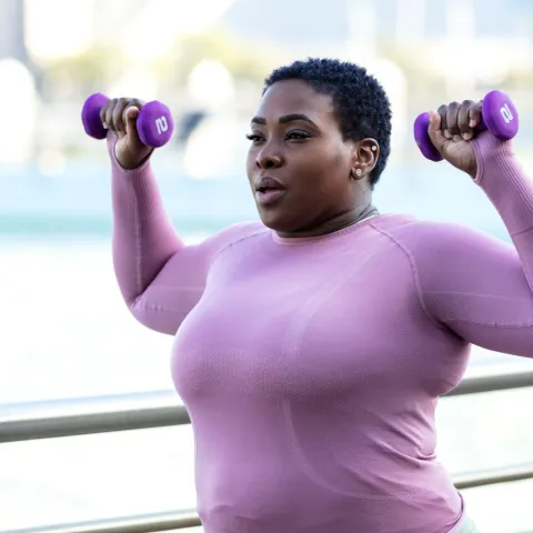 A Woman Exercises with Weights in a Park by the Water Front