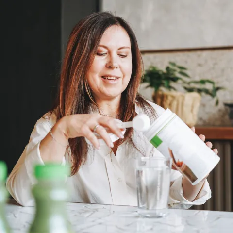 A Woman Scoops Protein Powder from a Container in Her Kitchen.