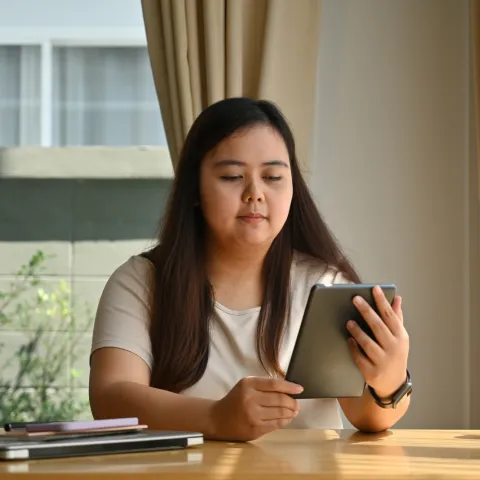 A Woman Reads a Tablet While Sitting at a Table at Home