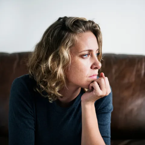 A Woman Sits in Her Home Staring Out the Window with a Serious Look On Her Face