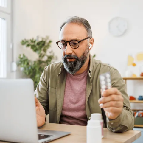 Man attending a virtual care appointment at home on laptop holding medication.
