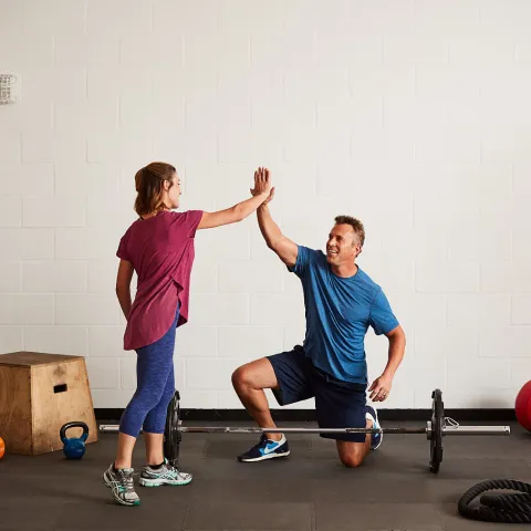 A Caucasian man and woman high-five while exercising at the gym.