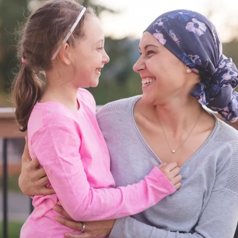 A mother and cancer survivor is sitting, with one arm around her daughter.