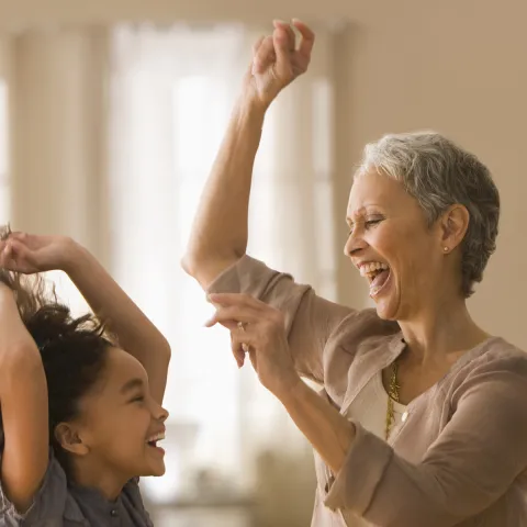 An elementary-aged girl and an older female relative dancing and smiling indoors
