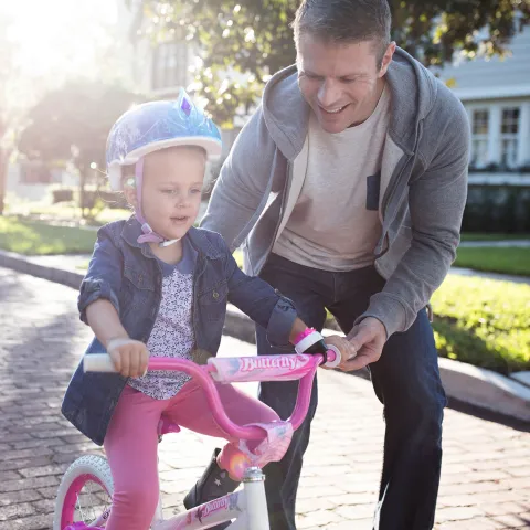 Father teaching his young daughter how to ride a pink bike in the street.