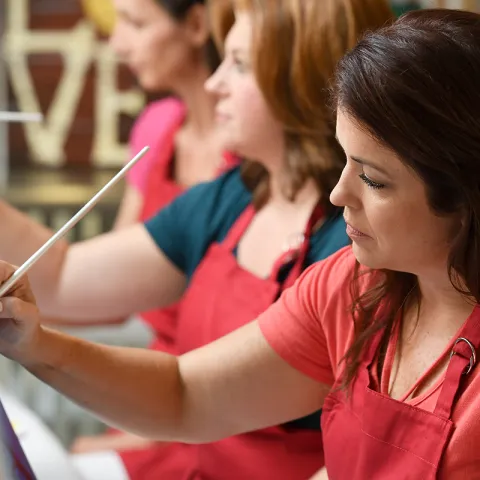 A woman wearing a smock and painting in an art class