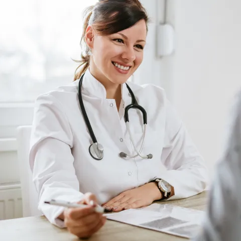 A friendly doctor meets a patient for the first time. They are both sitting at a desk, facing each other.