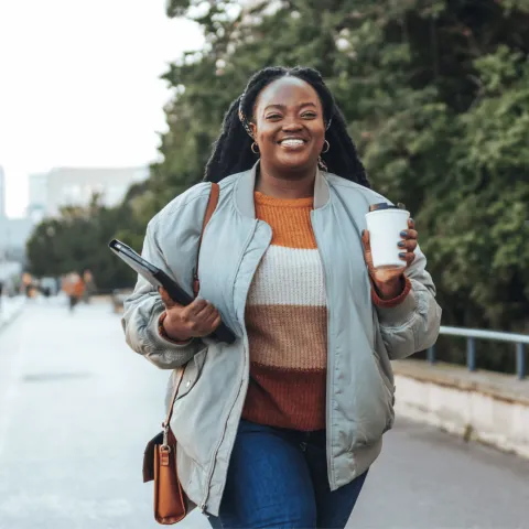 A Woman Walks Down a City Sidewalk with a Cup of Coffee