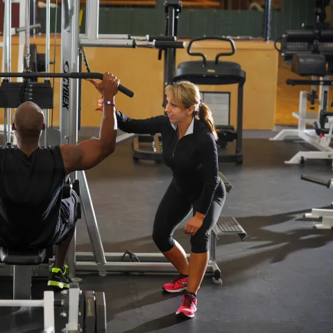 Female personal trainer coaching male trainee with a lat pulldown exercise.