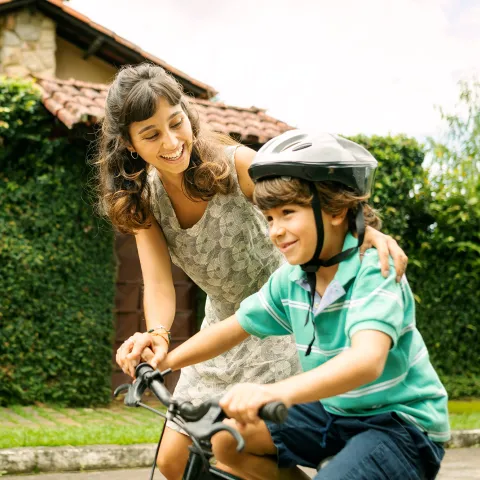 A mother helps her child learn to ride a bike.