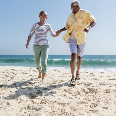 A couple holds hands while walking through sand on the beach.