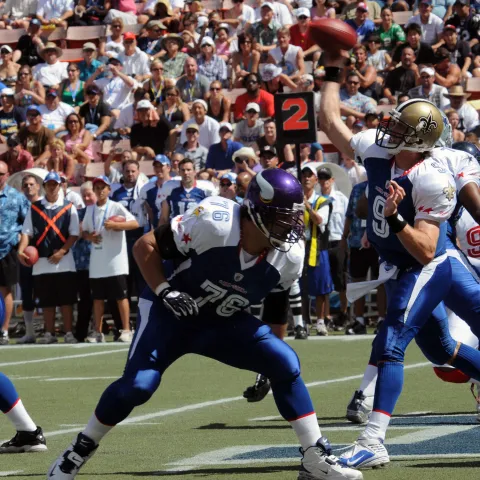 Football star, Drew Brees, passing the ball to a player.