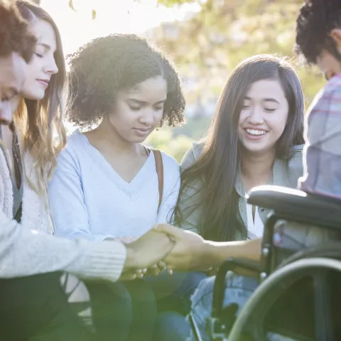 A group of friends holding hands and praying.