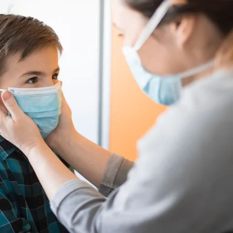 A mom puts a facemask on her son. 