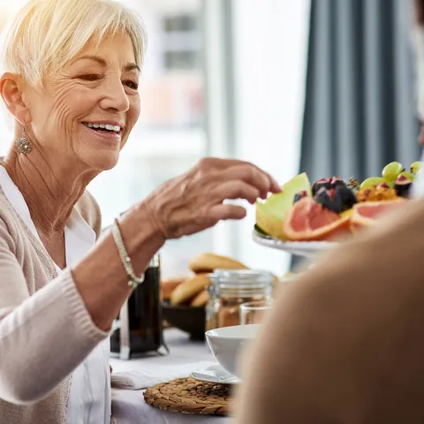 A senior woman picking fruit off from a fruit plate