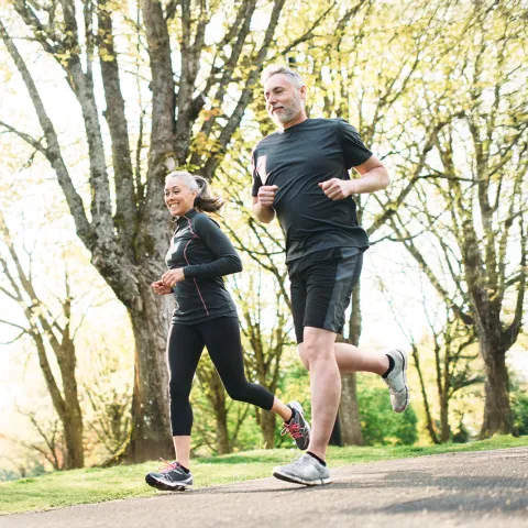 A Middle Aged Couple Jogs Through a Park