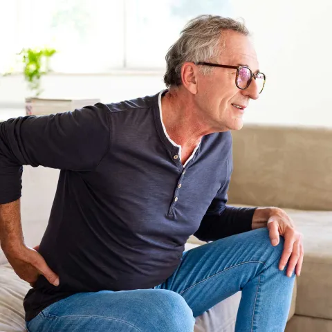 A senior gentleman showing discomfort while getting up from his couch