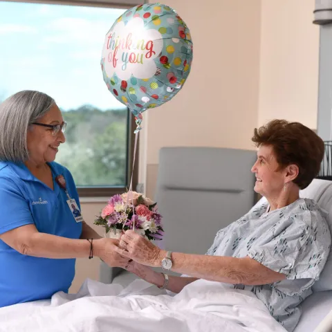Volunteer handing senior inpatient a gift of flowers and balloons.