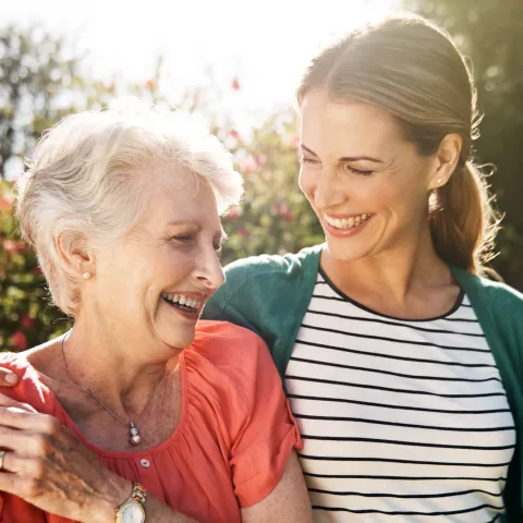 A senior woman with her adult daughter walking together outdoors.