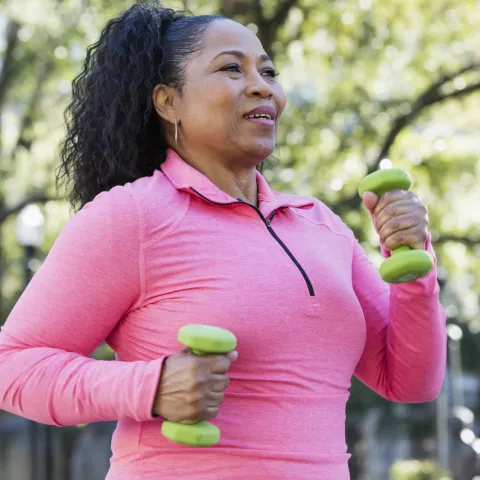 Woman walking outdoors and carrying small hand weights