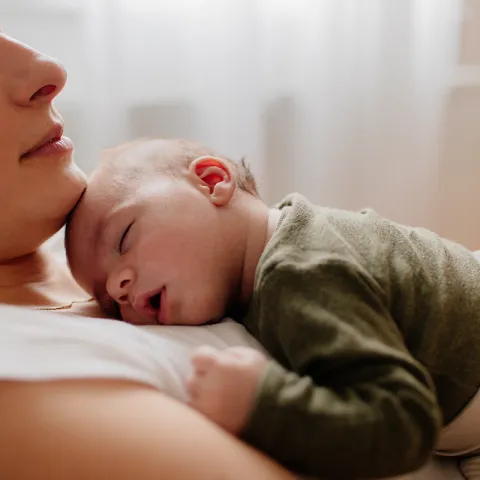 A mother closes her eyes and relaxes as her newborn sleeps on her chest.