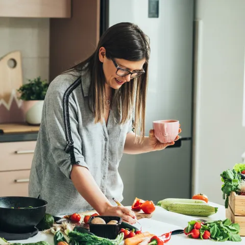 A woman writing down a recipe while in the kitchen and a lot of produce is on the counter.