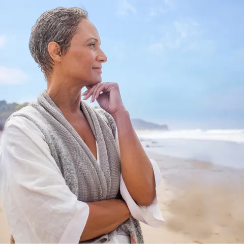 An adult woman stands on the beach and looks out at the ocean
