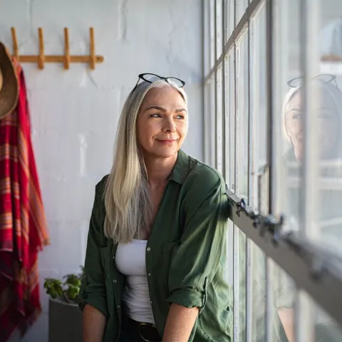 A mature woman sits at home and looks out a window