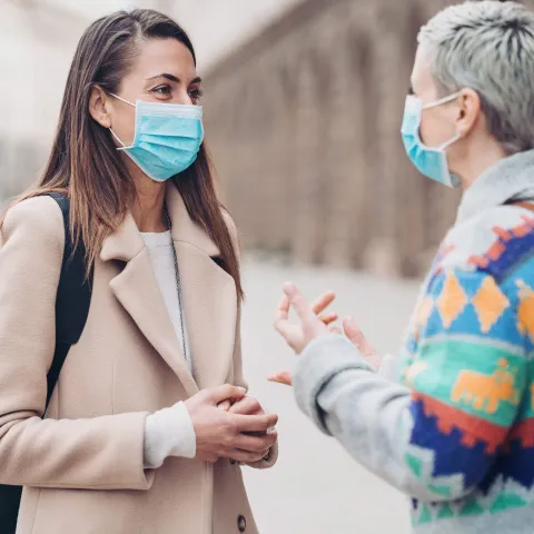 Two women wearing masks talking outside.