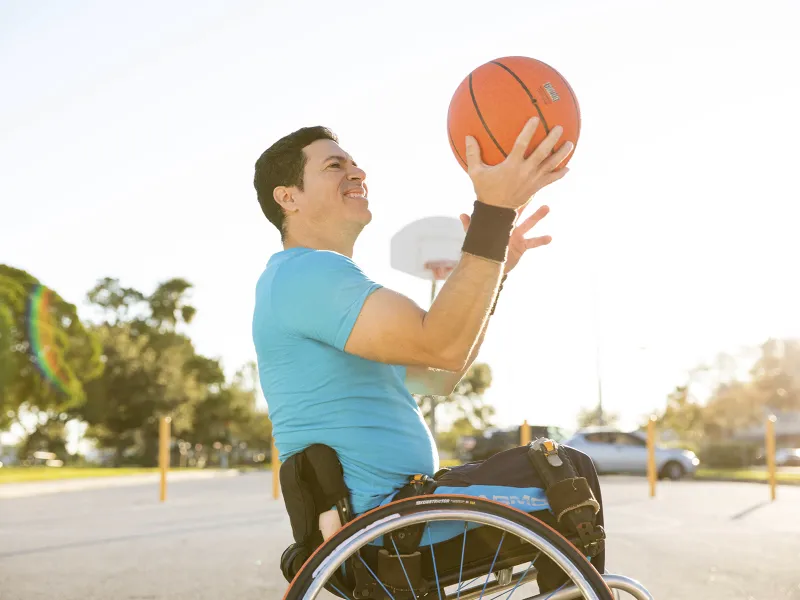 A Caucasian man in a wheelchair practices tricks with a basketball.