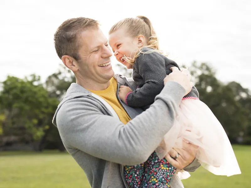 A Caucasian father and his young daughter play in the park together.