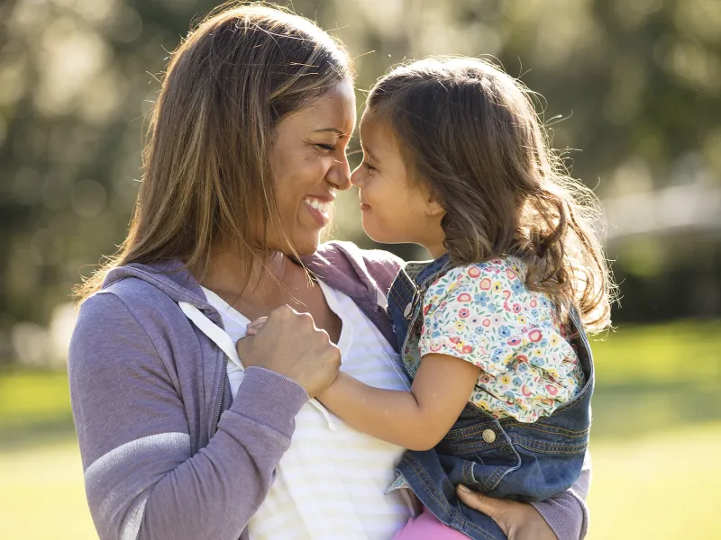 Mother and elementary-aged daughter giving eskimo kisses in the park. 