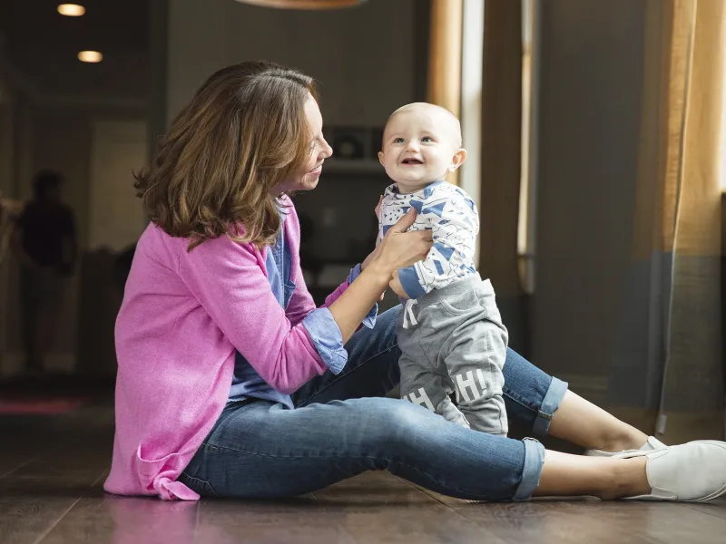 A young mother plays with her toddler on the floor.