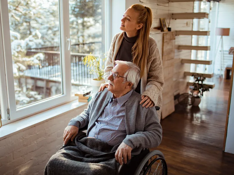 Caregiver Looks Out the Window with a Senior Patient at the Newly Fallen Snow.