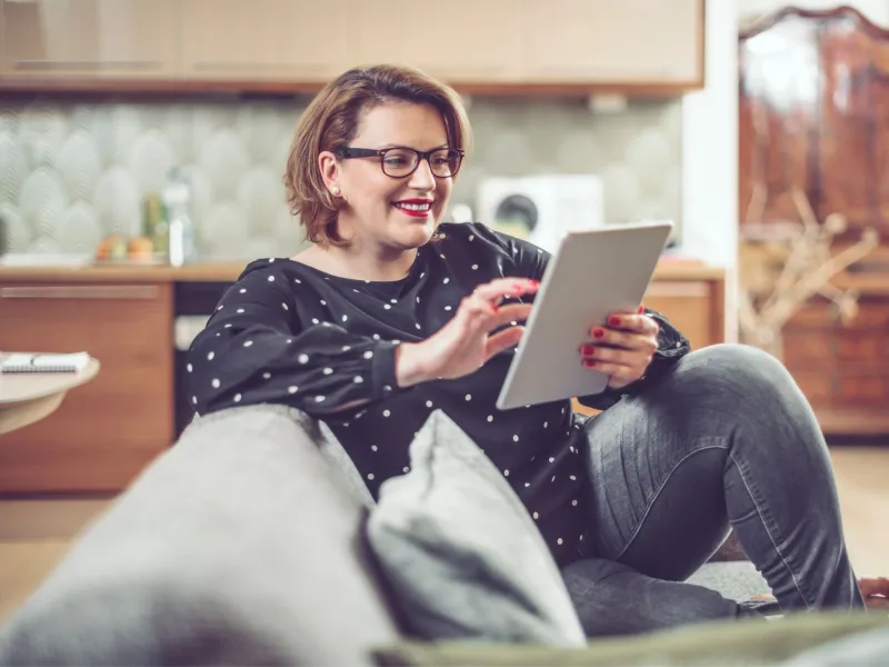 A Woman Smiles as She Looks at Content of Her Tablet at Home.