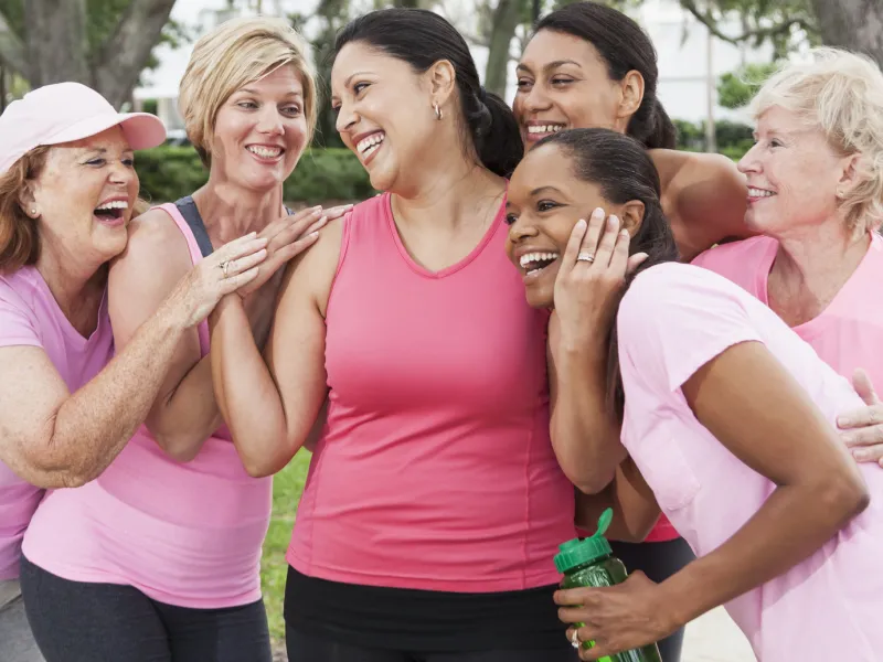 A group of friends, all wearing pink and hugging a woman in the venter, to support a breast cancer survivor.