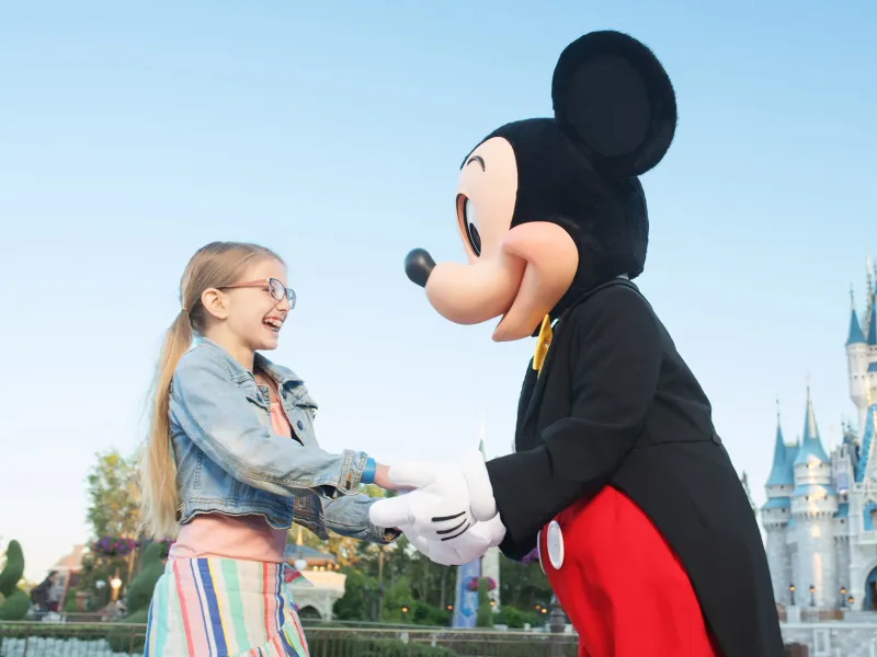 Mickey Mouse holding a girls hands in front of Cinderella's Castle.