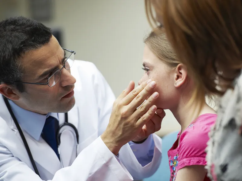 A male doctor examines the eyes of a young girl.