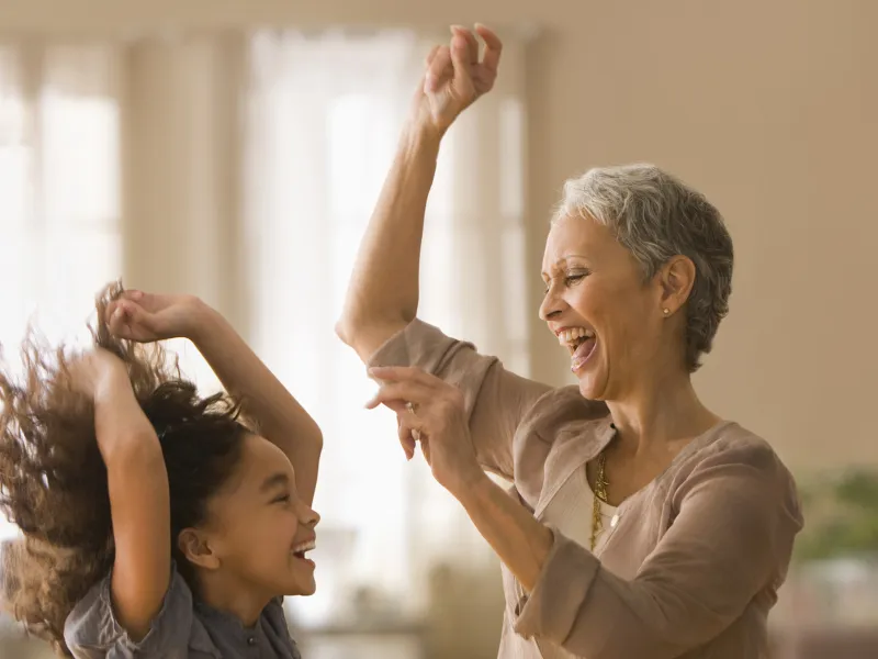 An elementary-aged girl and an older female relative dancing and smiling indoors
