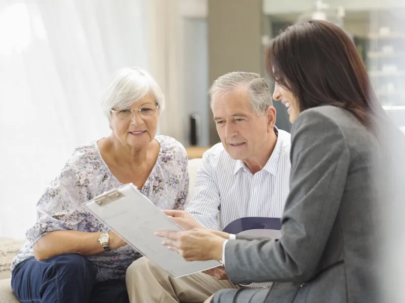 A female hospital staff member discusses information with an elderly couple.
