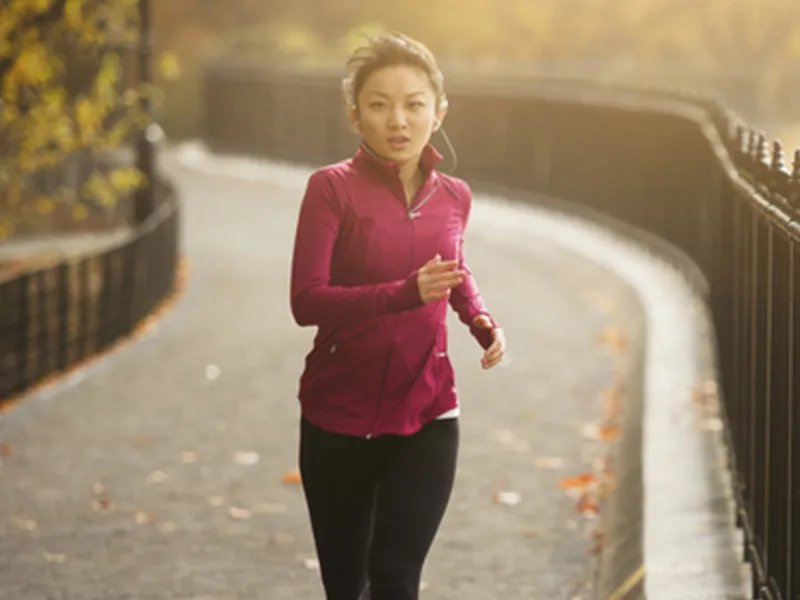 A young Asian woman jogs in the park on a fall afternoon.