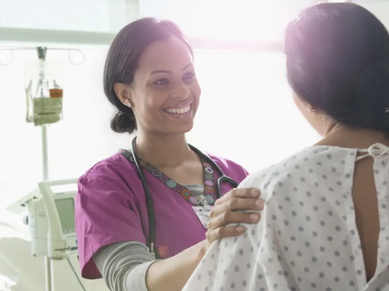 A female African American nurse consoles a woman in a hospital gown.