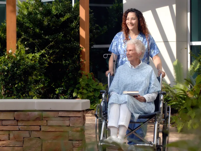 Elderly woman in a wheelchair with a nurse in a garden.