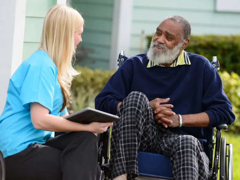 Elderly man in a wheelchair outside speaking to a nurse.