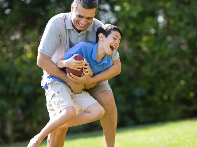 A father and son play football outdoors.