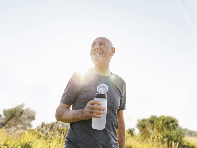 An older man takes a water break during a sunny outdoor hike