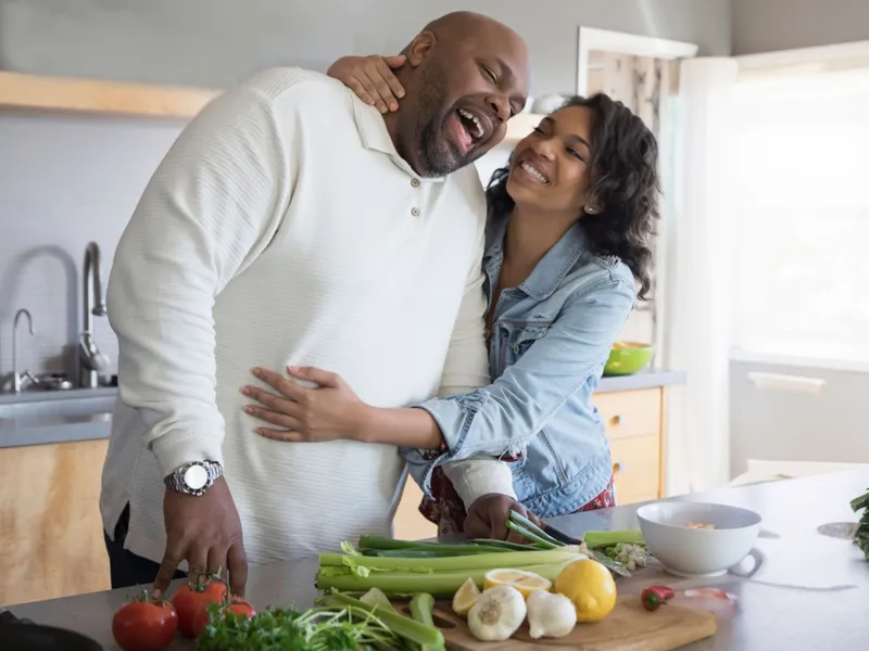 A couple hugging each other while cooking on the kitchen