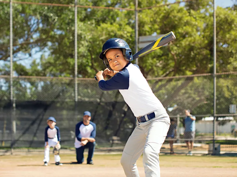 A boy playing baseball in the park with his father and his brother.