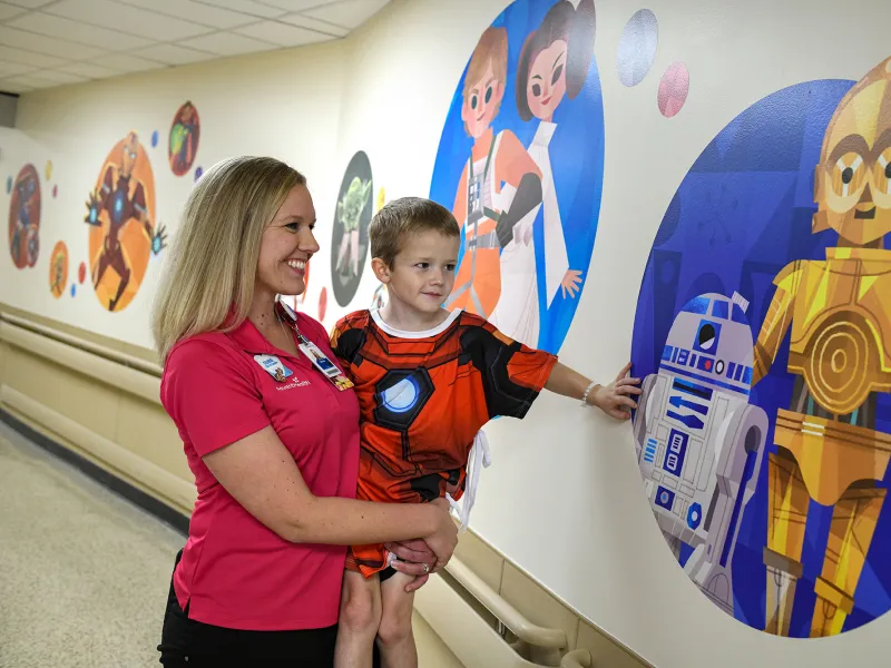 Boy patient with AdventHealth for Children employee looking at a wall with C-3PO and R2-D2