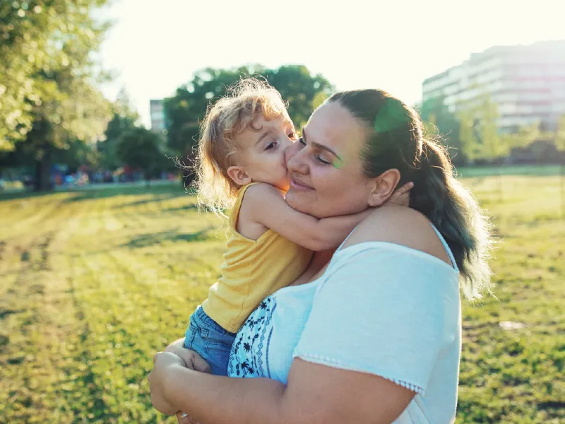 Woman standing in a field holding her child.